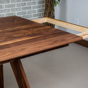May include: A wooden dining table with a leaf extension. The table is made of walnut wood and has a natural finish. The leaf is made of maple wood and is attached to the table with a metal track.