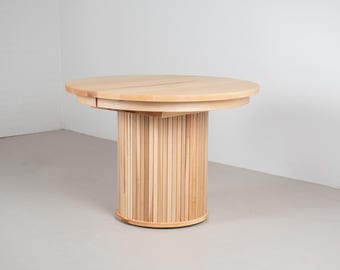 May include: A round wooden table with a slatted base. The table top is made of light wood and the base is made of a darker wood.