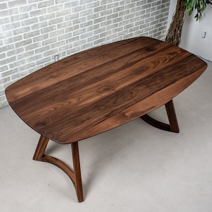 May include: A dark brown oval-shaped wooden table with a unique curved base. The table top is made of solid wood with a natural grain pattern.