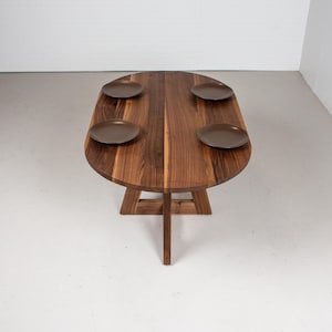 May include: A wooden oval table with a natural wood finish and four brown plates on top. The table has a unique, triangular base.