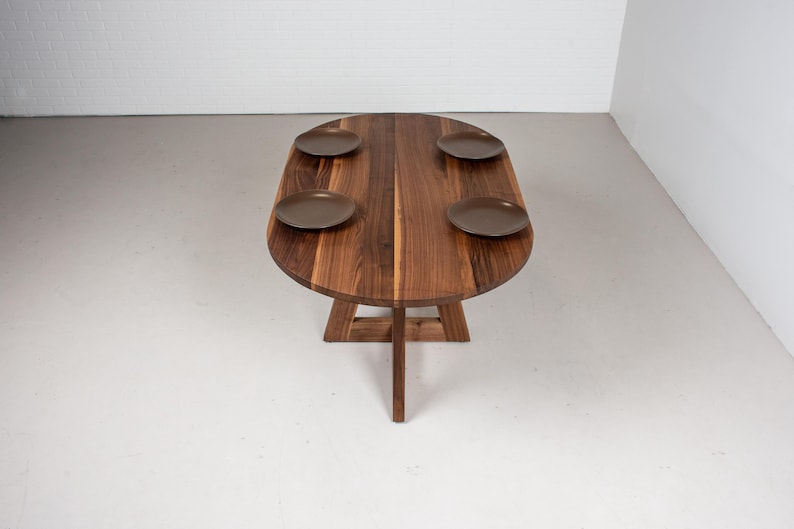 May include: A wooden oval table with a natural wood finish and four brown plates on top. The table has a unique, triangular base.
