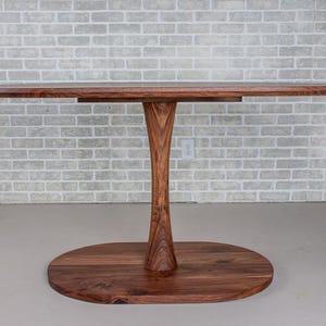 May include: A wooden oval table with a single pedestal base. The table top and base are made of dark wood.