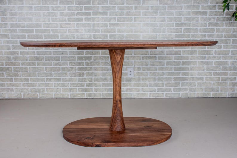 May include: A wooden oval table with a single pedestal base. The table top and base are made of dark wood.