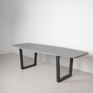 May include: A gray, oval-shaped table with black, angular legs. The table has a light gray surface and is supported by two black, U-shaped legs. The design is modern and minimalist, suitable for a dining or conference setting.