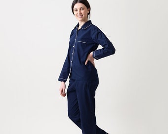 May include: A navy blue pajama set with white piping. The top has a button-down front and long sleeves. The pants have a straight leg.