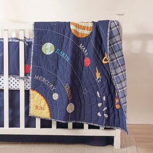 May include: A blue and yellow baby quilt with a space theme. The quilt features a sun, planets, and stars. The text on the quilt reads "Sun", "Mercury", "Venus", "Earth", "Mars".