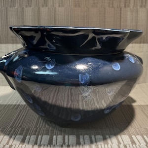 May include: A dark blue ceramic bowl with a wide, ruffled rim. The bowl has a rounded body with blue polka dots and a glossy finish. The bowl is likely used for decorative purposes.