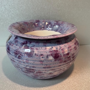 Peut inclure: Un bol en céramique avec un large bord évasé et un corps rond. Le bol est principalement lavande avec un motif tacheté de violet foncé et de blanc. L'intérieur est de couleur blanc crème.