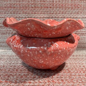 Peut inclure: Un pot en céramique rose avec un glaçage blanc moucheté. Le pot a un dessus festonné et un fond arrondi.
