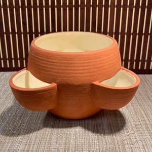 May include: A terracotta strawberry planter with a matte, textured exterior and a smooth, cream-coloured glazed interior. The vessel features a large central opening and three smaller, rounded side pockets for planting, all connected to a single base.