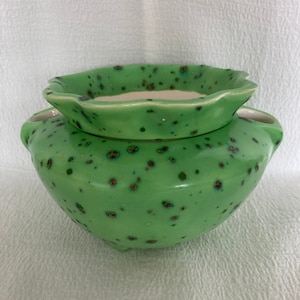 May include: A green ceramic planter with a speckled glaze. The planter has a removable top with a scalloped edge.