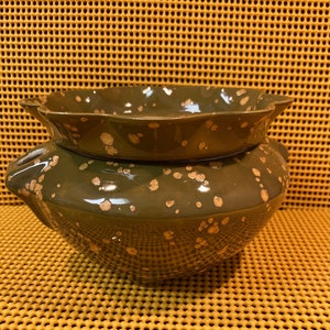 May include: A two-piece ceramic pottery set in a dark green glaze with speckled gold accents. The top piece has a scalloped edge, and the bottom piece has two handles. The set is likely for decorative or functional use.