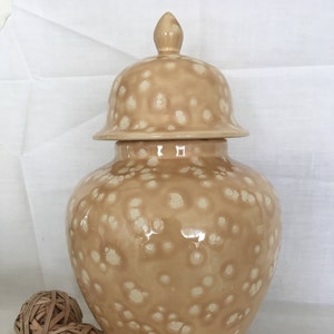 May include: A large, beige ceramic ginger jar with a white speckled pattern. The jar has a domed lid with a finial.