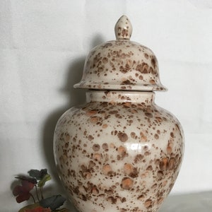 May include: A white ceramic jar with a lid, decorated with brown and orange speckles. The jar has a round body and a wide mouth. The lid has a knob on top.