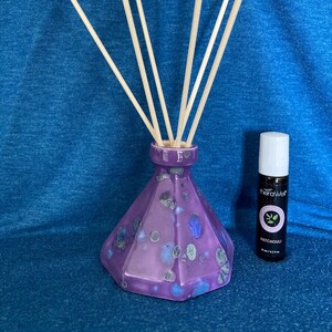 May include: Purple ceramic diffuser bottle with a geometric design and wooden diffuser sticks. The bottle is filled with essential oil and has a label that reads "theraWell Patchouli 10 ml / 0.33 fl oz".