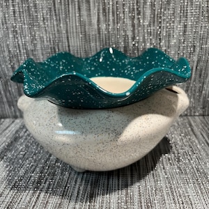 May include: A two-piece ceramic decorative bowl set. The top bowl is teal with a ruffled edge and white speckles. The bottom bowl is white with black speckles. The bowls are designed to nest together.