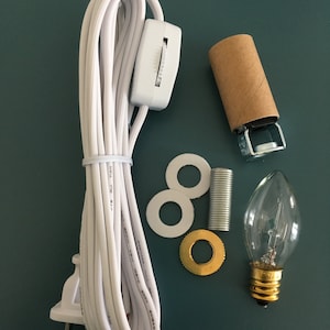 May include: A white electrical cord with a plug, inline switch, and a light bulb socket. The cord is coiled and includes a white plastic inline switch. The socket is a standard light bulb socket with a brown paper covering. The kit also includes a white plastic washer, a gold metal washer, and a silver metal threaded rod.