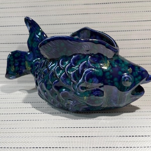 May include: A blue and green ceramic fish shaped bowl with a glazed finish. The fish has a detailed design of scales and fins.