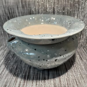 May include: A white ceramic mug with a black handle and the text "But First, Coffee" in a black, bold font. The mug is on a white surface. The mug is approximately 10 cm tall.