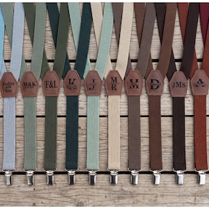 Pode incluir: Uma coleção de suspensórios em várias cores, incluindo azul, verde, castanho e bordô. Cada suspensório tem um remendo de couro com iniciais ou nomes como "PAUL" e "David". Os suspensórios têm clipes prateados.