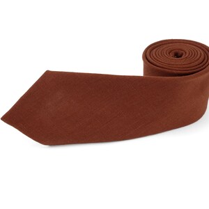 Op de afbeelding: Een opgerolde, bruine stropdas met een puntige punt. Gemaakt van een textuurstof, gepresenteerd tegen een witte achtergrond. Een klassiek accessoire voor formele of zakelijke kleding. De stropdas heeft een rijke, aardse tint.