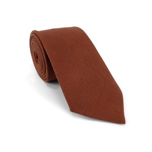 Op de afbeelding: Een opgerolde stropdas in een warme, roodbruine tint. De stropdas is gemaakt van een textuurstof en wordt gepresenteerd op een witte achtergrond. Een klassiek accessoire voor formele of zakelijke kleding.