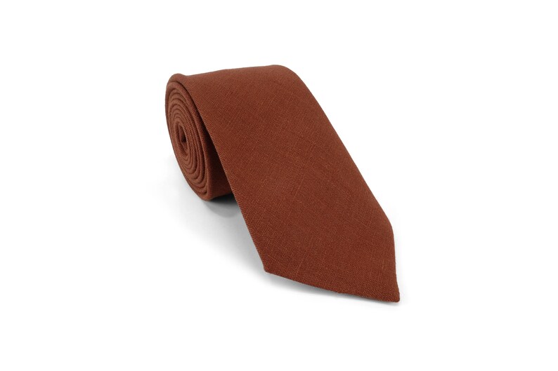 Op de afbeelding: Een opgerolde stropdas in een warme, roodbruine tint. De stropdas is gemaakt van een textuurstof en wordt gepresenteerd op een witte achtergrond. Een klassiek accessoire voor formele of zakelijke kleding.