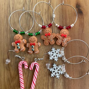 May include: A collection of holiday-themed earrings featuring silver-tone hoops and hooks. The set includes gingerbread men with red bows, red and white striped candy canes, and white snowflake charms accented with green, red, and clear beads.