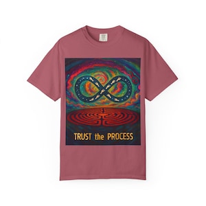 May include: Dusty rose t-shirt featuring a colorful graphic. The graphic includes an infinity symbol with footprints, a maze, and the text "TRUST the PROCESS". The design has a cosmic, spiritual theme.