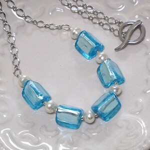 May include: A silver chain necklace with blue and white glass beads. The necklace has a silver clasp.