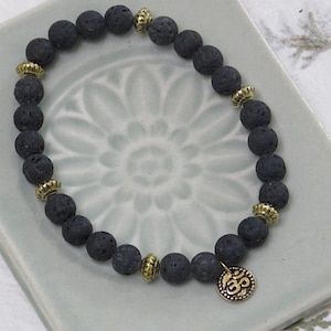 May include: Black lava rock beaded bracelet with gold accents and an Om charm.