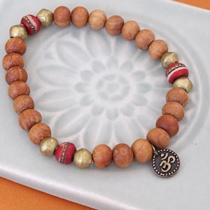 May include: A wooden beaded bracelet with gold and red accents. The bracelet has a charm with the Om symbol.