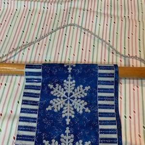 May include: A blue and white snowflake patterned fabric banner hanging from a wooden dowel rod with a white rope.