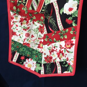 May include: A red, green, and white patchwork table runner with a floral pattern. The runner has a red border with gold stitching.