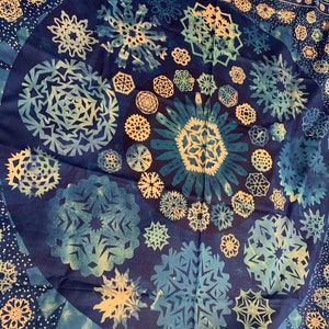 May include: A blue fabric tapestry featuring a circular design of white snowflakes. The snowflakes are of various sizes and shapes, creating a visually appealing pattern.