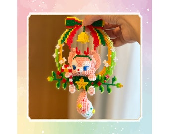 May include: A pink and white beaded Christmas bauble shaped like a cartoon animal wearing a Santa hat and holding a candy cane. The bauble is hanging from a green and yellow beaded wreath with a red bow and a yellow bell.
