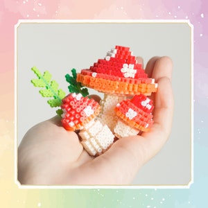 Op de afbeelding: Drie rode en witte paddenstoelvormige kralenkunst met een groene, bladerige stengel. De paddenstoelen zijn gemaakt van kleine, kleurrijke kralen en worden in de hand van een persoon gehouden.