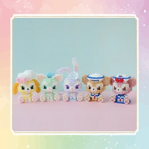 May include: Five small, colorful, beaded figurines of cartoon characters. The characters are a yellow dog, a green cat, a purple bunny, a brown bear, and a pink bear. Each character is wearing a hat and has a different expression.