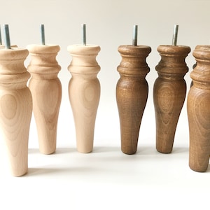 Pode incluir: Um conjunto de pés de móveis de madeira em tons naturais e castanhos. Cada pé tem um parafuso roscado para fixação. Os pés torneados apresentam um design clássico e decorativo, adequados para restauração ou construção de móveis.