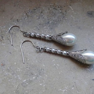 May include: A pair of silver dangle earrings with white pearl drops. Each earring features a delicate silver design around the pearl.