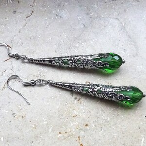 May include: A pair of silver dangle earrings with green crystal teardrop accents. The earrings have a filigree design.