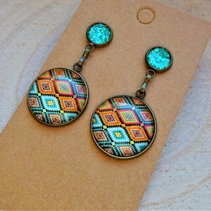 Op de afbeelding: Een paar oorhangers met een rond, kleurrijk geometrisch patroon en een turquoise glitteraccent.