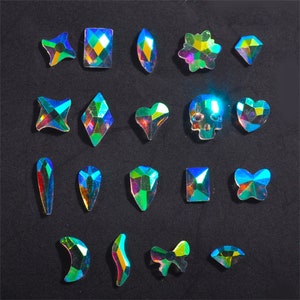 Könnte beinhalten: Sortiment aus schillernden Strasssteinen in verschiedenen Formen und Größen, darunter Herzen, Sterne, Schädel, Schmetterlinge und geometrische Formen.