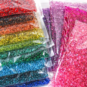 May include: Assortment of colourful, transparent, water beads in individual plastic bags. The beads are arranged in a rainbow pattern, with red, orange, yellow, green, blue, and purple beads.