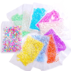 May include: Assortment of colorful, iridescent, and clear rhinestones in individual clear plastic bags. The rhinestones are various sizes and shapes.