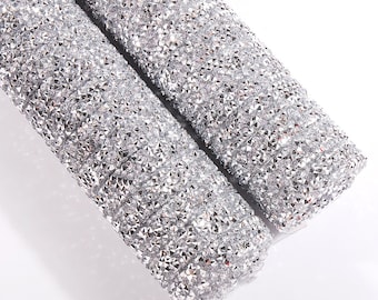 May include: Two rolls of silver glitter fabric with a diamond-like texture. The fabric is rolled up and the ends are visible.
