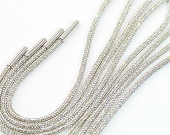 May include: A set of seven silver shoelaces with clear rhinestones. The shoelaces are flat and have a smooth, shiny finish. The rhinestones are evenly spaced and create a sparkling effect.