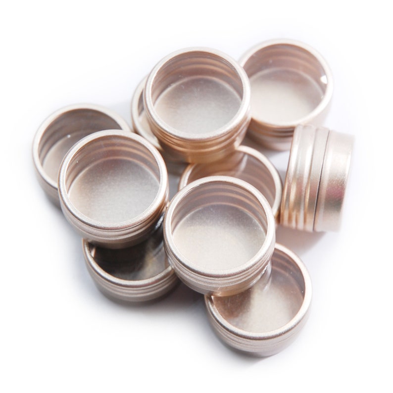 May include: A pile of small, round, gold-coloured metal containers with clear lids. The containers are stacked on top of each other.