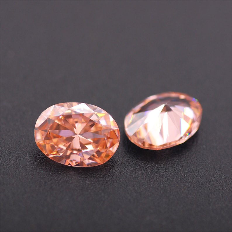 May include: Two oval-shaped, light pink gemstones with a faceted cut. The gemstones are set against a black background.