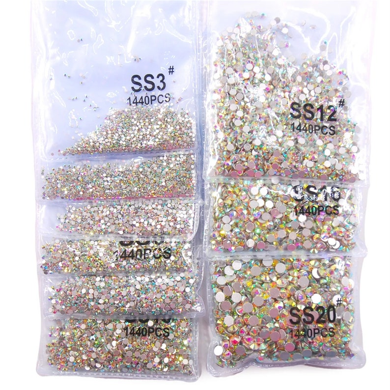 May include: Assortment of clear iridescent rhinestones in various sizes, packaged in individual clear plastic bags. Each bag contains 1440 pieces and is labeled with the size, "SS3", "SS12", "SS16", and "SS20".